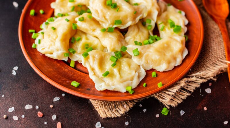 The boiled made dumplings with a stuffing with oil and green onions on a dark table